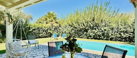 A covered outdoor area with a pool, seating, and a view of the surrounding greenery.
