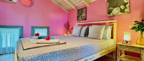 A bedroom with a wooden ceiling, pink walls, a bed with floral bedding, and a nightstand with a vase.