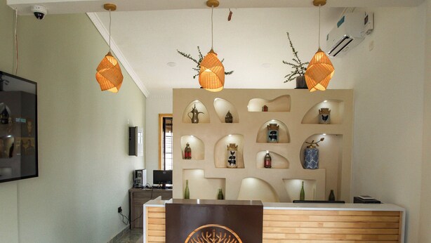 A reception area with a wooden reception desk, a teal sofa, and a decorative wall with shelves. - The Choate Boutique Hotel & Restaurant (Kampala)