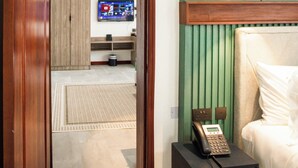 A hotel room with a bed, a bedside table with a telephone, a television on the wall, and a green accent wall. - The Choate Boutique Hotel & Restaurant (Kampala)