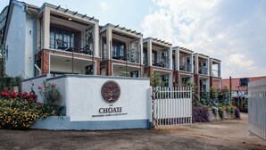 A hotel with a white facade, multiple balconies, and a sign indicating it is a boutique hotel and restaurant. - The Choate Boutique Hotel & Restaurant (Kampala)