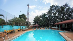 A swimming pool with a clear blue water, surrounded by lounge chairs and a covered seating area. - The Choate Boutique Hotel & Restaurant (Kampala)