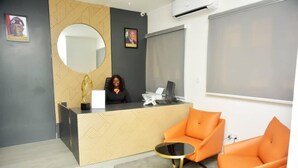 Un área de recepción con diseño moderno, que incluye un mostrador de recepción, un espejo redondo y sillas color naranja.