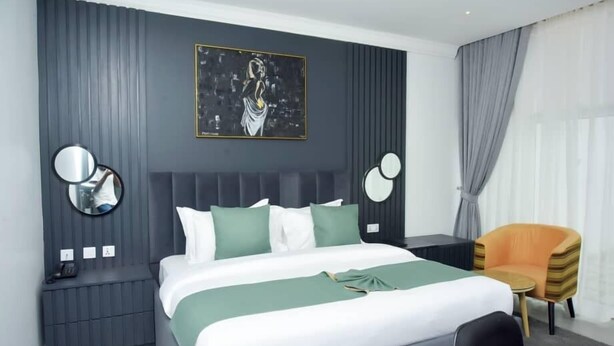 Una habitación de hotel moderna con una cama grande, una mesita de noche con teléfono, una silla y un cuadro en la pared.