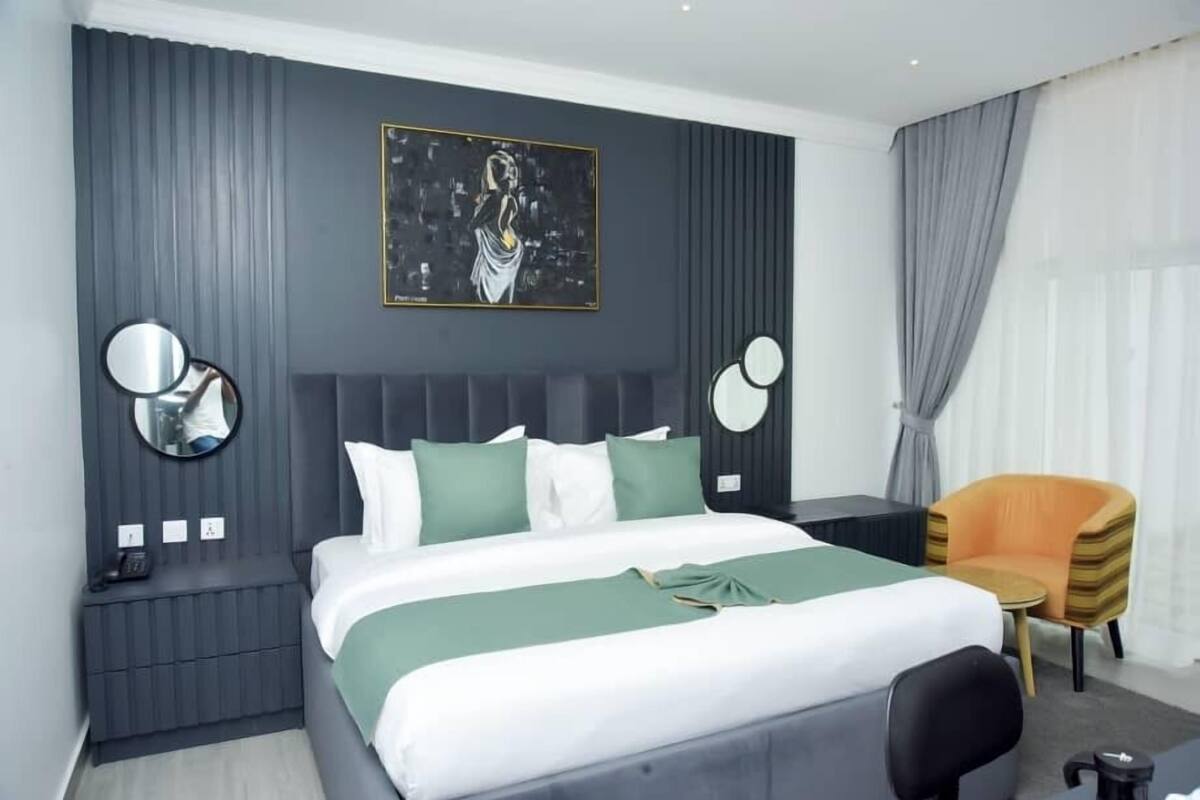 Ein modernes Hotelzimmer mit einem großen Bett, einem Nachttisch mit Telefon, einem Sessel und einem Bild an der Wand.