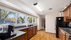 A modern kitchen with wooden cabinets, a black refrigerator, and a coffee maker on the counter. - Poolside Palisade - A Fun Family Retreat for 6 (Marquette Heights)