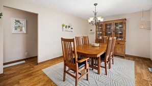 A dining room with a wooden table and chairs, a chandelier, and a cabinet with glass doors. - Poolside Palisade - A Fun Family Retreat for 6 (Marquette Heights)