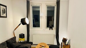 A modern living room with a black sofa, a wooden coffee table, and black ottomans. There is a radiator under the window, a lamp, and a bookshelf with books and decorative items. - Charming townhome with 2 bedrooms and AC, WiFi in lovely Suffolk Park (Suffolk Park)