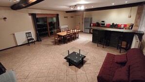 Un salón espacioso con una mesa de comedor y sillas, una cocina con refrigerador y microondas, y un sofá rojo.