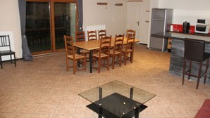 Un comedor con una mesa y sillas de madera, una mesa de centro con cubierta de vidrio y una cocina equipada con refrigerador y microondas.