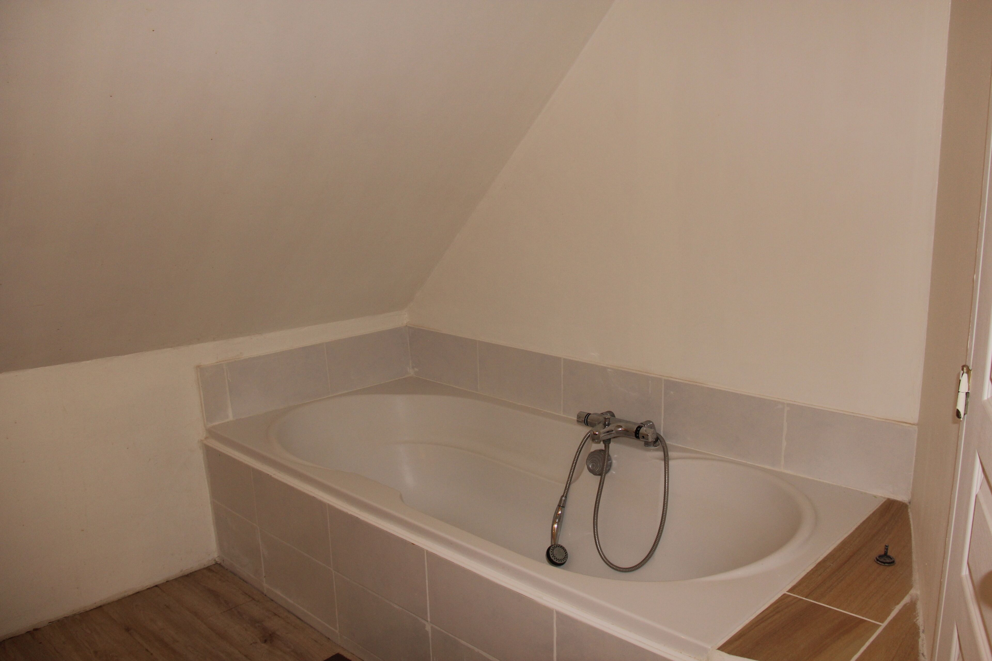 Une salle de bain avec une baignoire sur pieds, des murs carrelés et un plancher en bois.