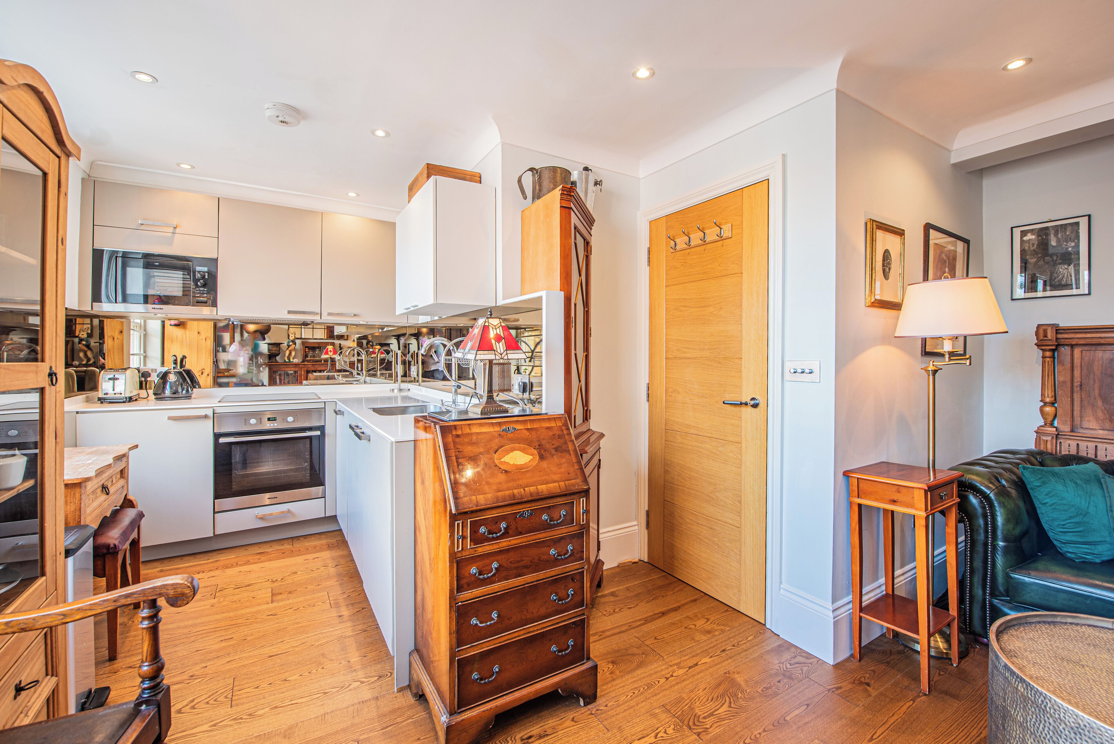 A modern kitchen with built-in appliances, a wooden chest of drawers, and a dining area with a green sofa.