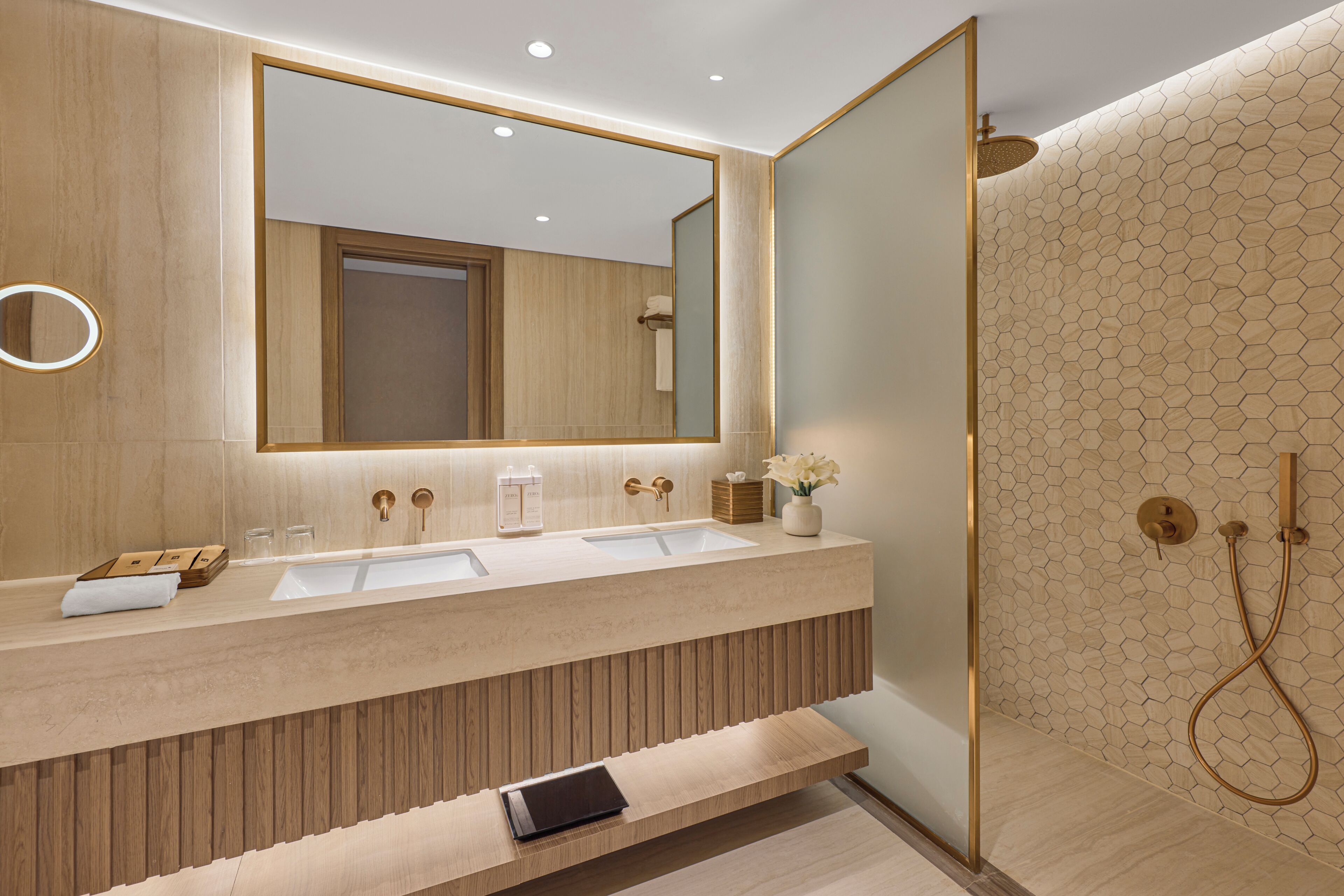 A modern bathroom with a large mirror, two sinks, a shower, and a wooden vanity.