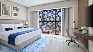 A hotel room with a large bed, a desk with a TV, a chair, and a window with a view of buildings. - Makarem Burj Al Madinah Hotel and Suites (Madinah)