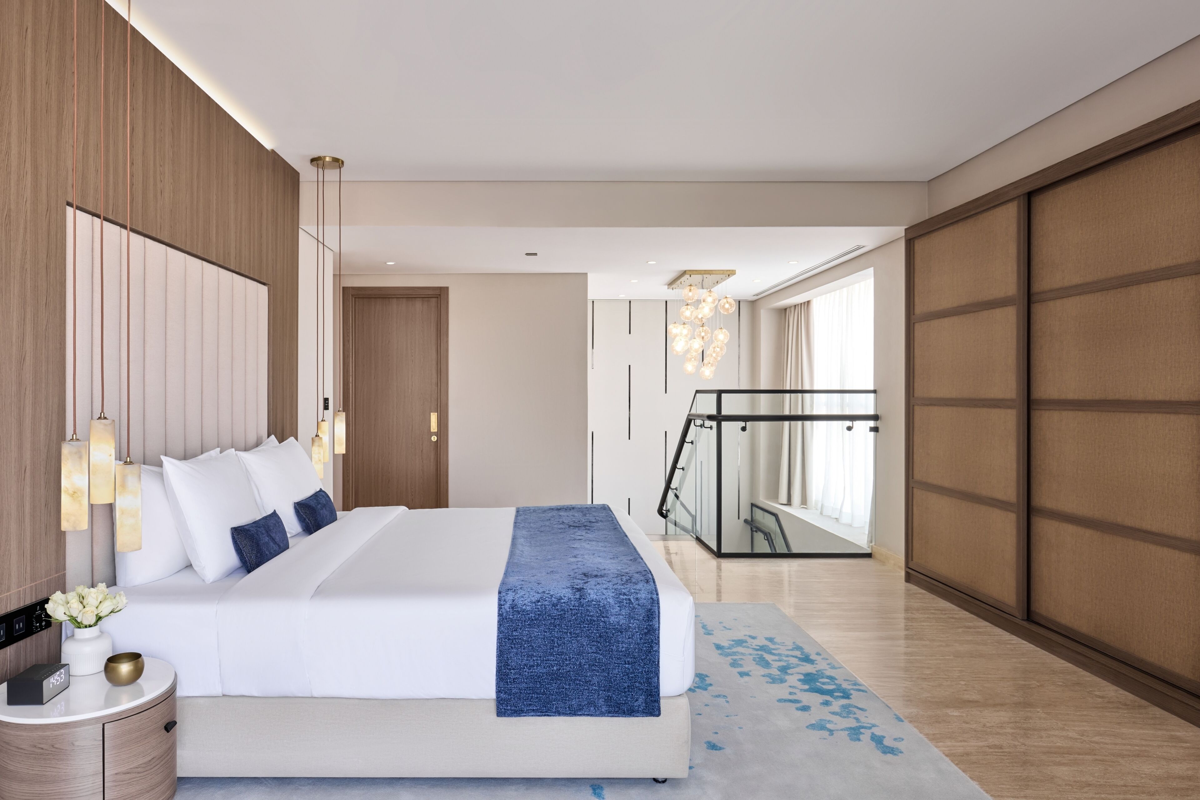 A modern bedroom with a large bed, bedside tables, a nightstand, a blue throw blanket, and a view of a balcony.
