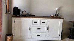 Un meuble blanc avec des tiroirs et un plan de travail, une petite orchidée en pot et un tableau encadré accroché au mur.