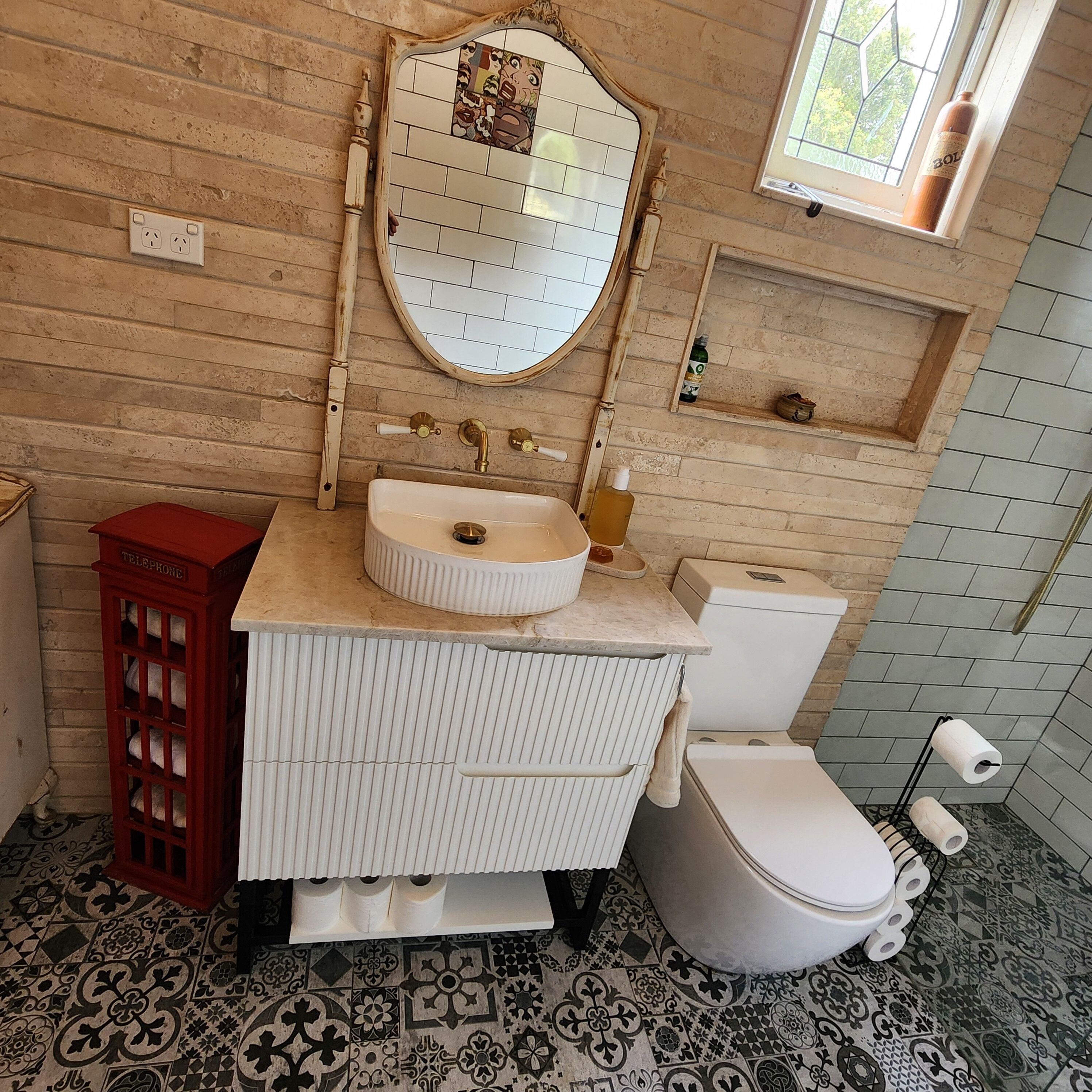 A bathroom with a wooden wall, a round mirror, a white sink, a toilet, and patterned floor tiles.