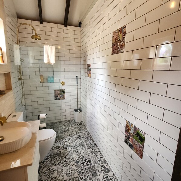 A bathroom with white subway tiles, a patterned floor, a toilet, a sink, and a shower with a gold showerhead.