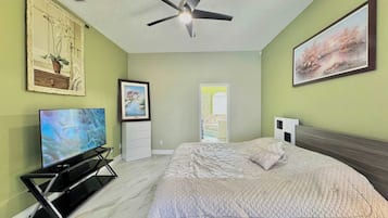 Een slaapkamer met een bed, een plafondventilator, een televisie en kunstwerken aan de muren.