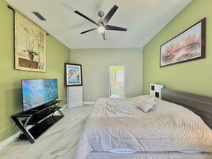 Een slaapkamer met een bed, een plafondventilator, een televisie en kunstwerken aan de muren.