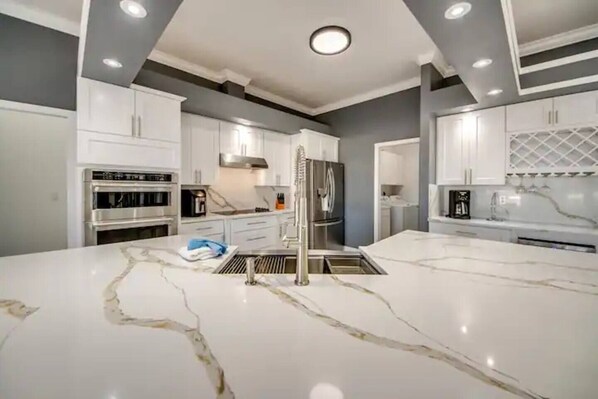 A modern kitchen with white cabinetry, stainless steel appliances, and a marble island.