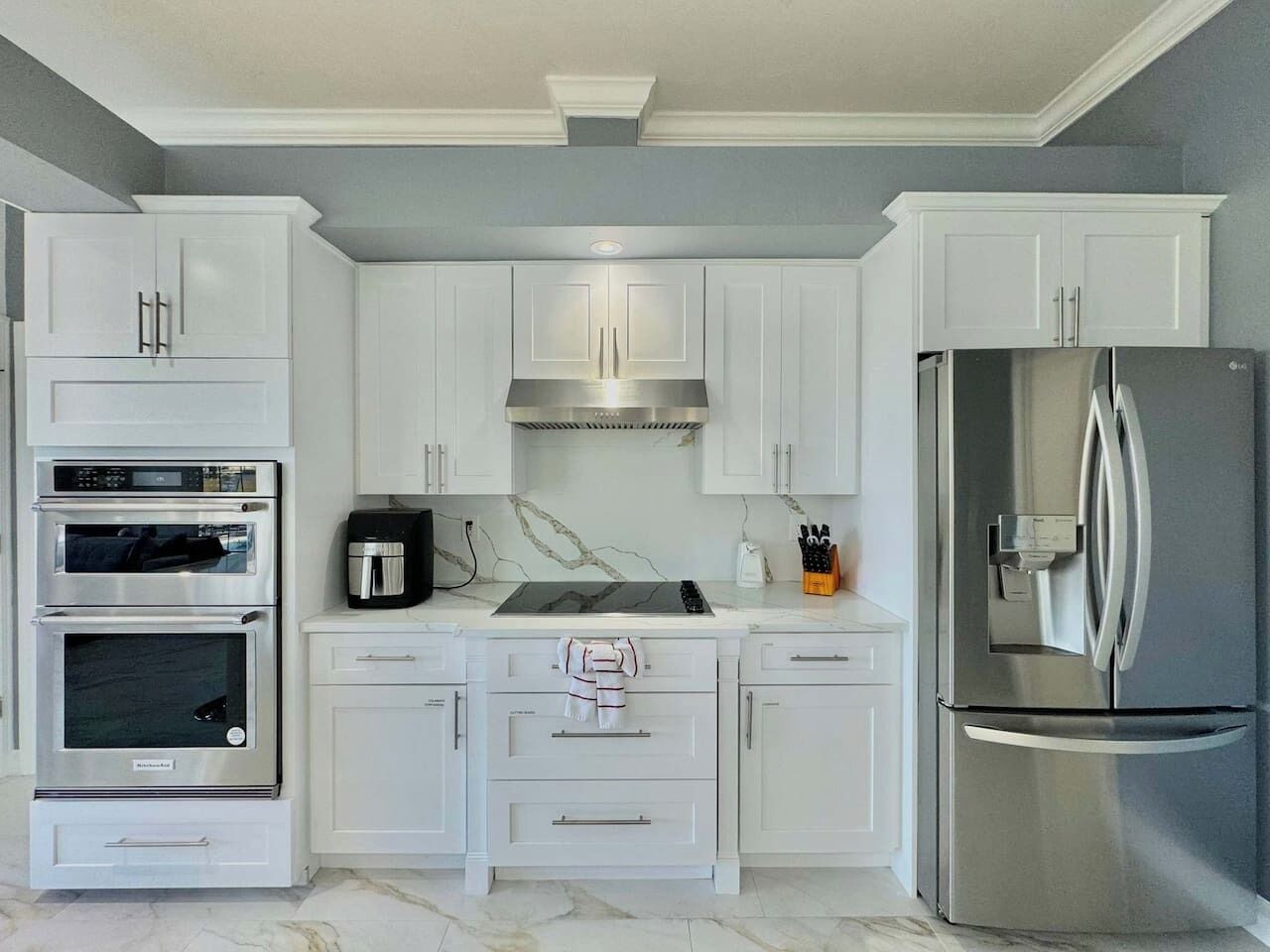 A kitchen with white cabinets, a stainless steel refrigerator, a double oven, a coffee maker, and a microwave.