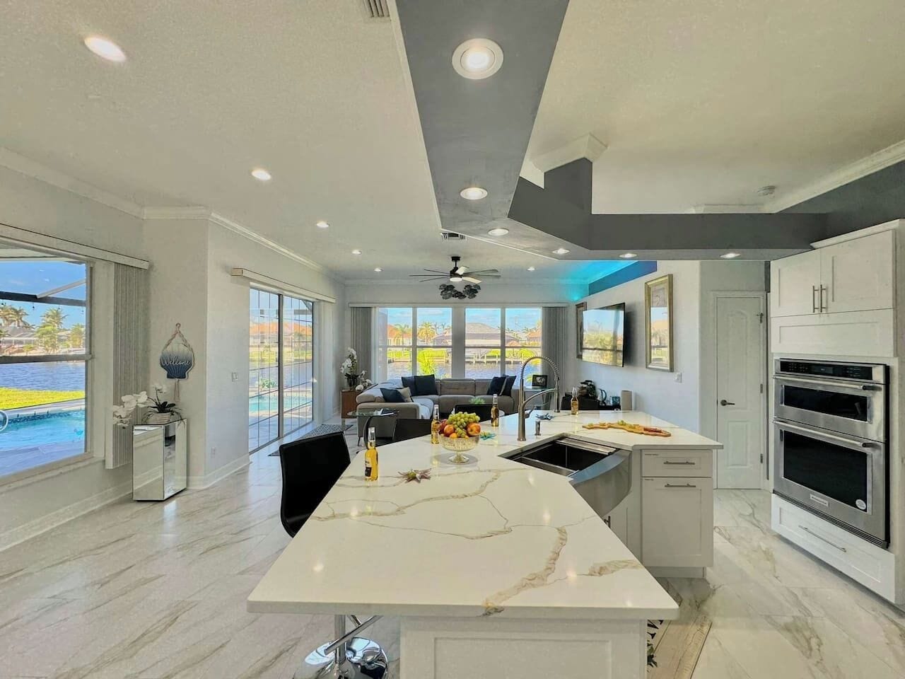 A modern kitchen with a marble island, built-in oven, and large windows overlooking a pool.