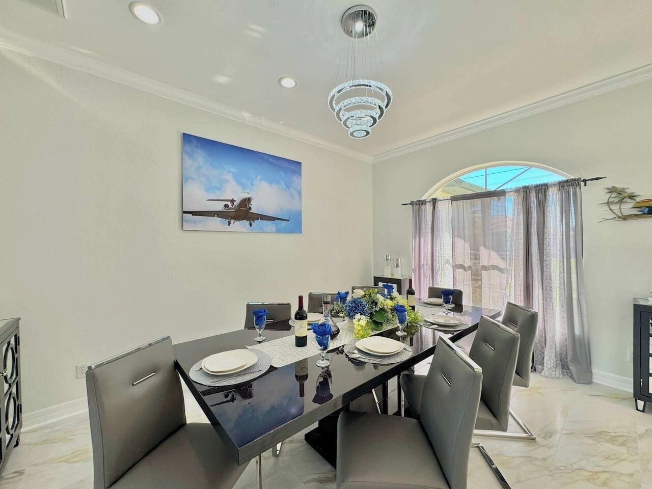 Un espace repas comprenant une longue table, des chaises, un lustre et un tableau accroché au mur.