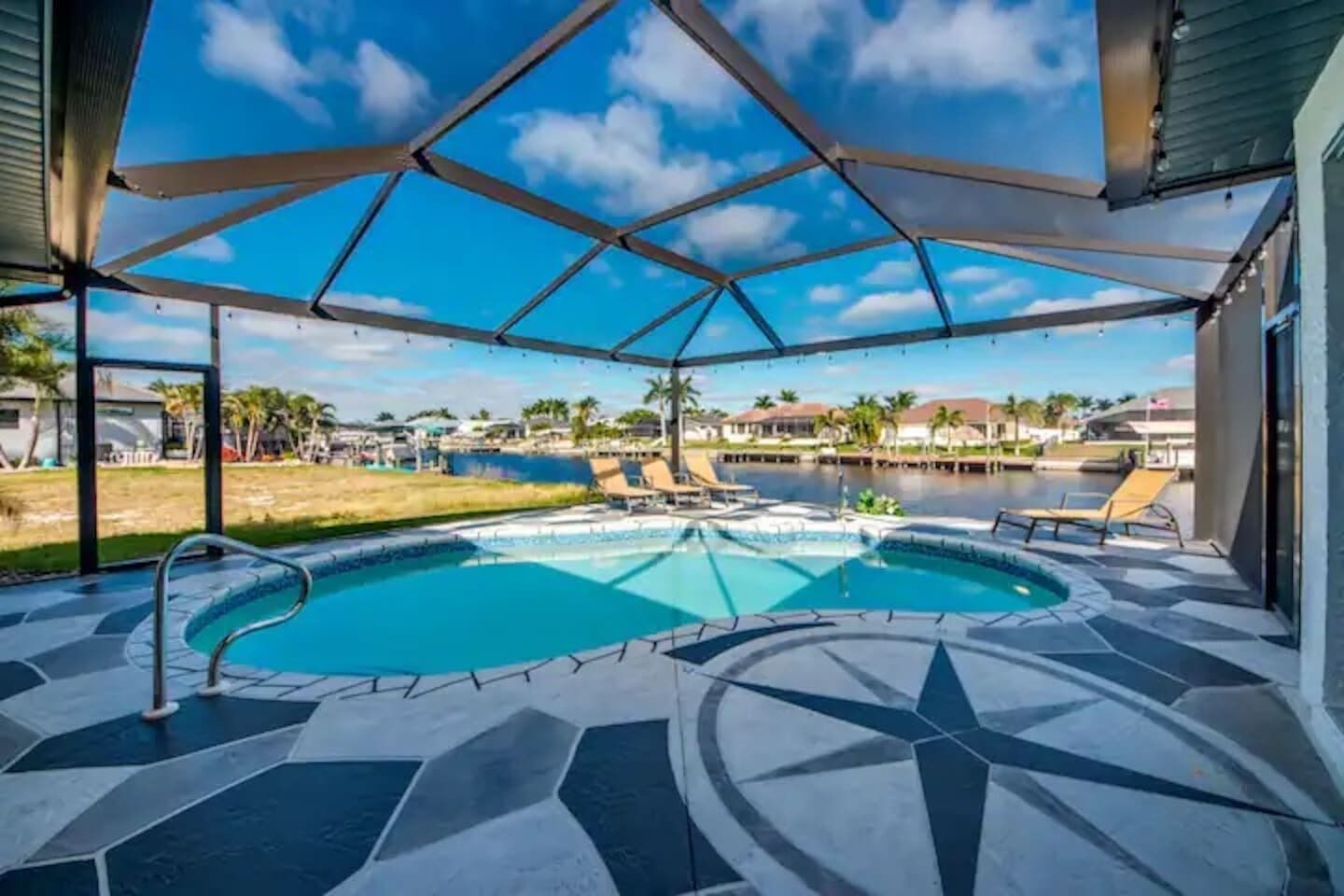 A swimming pool with a geometric tile design, surrounded by lounge chairs and a covered patio area.