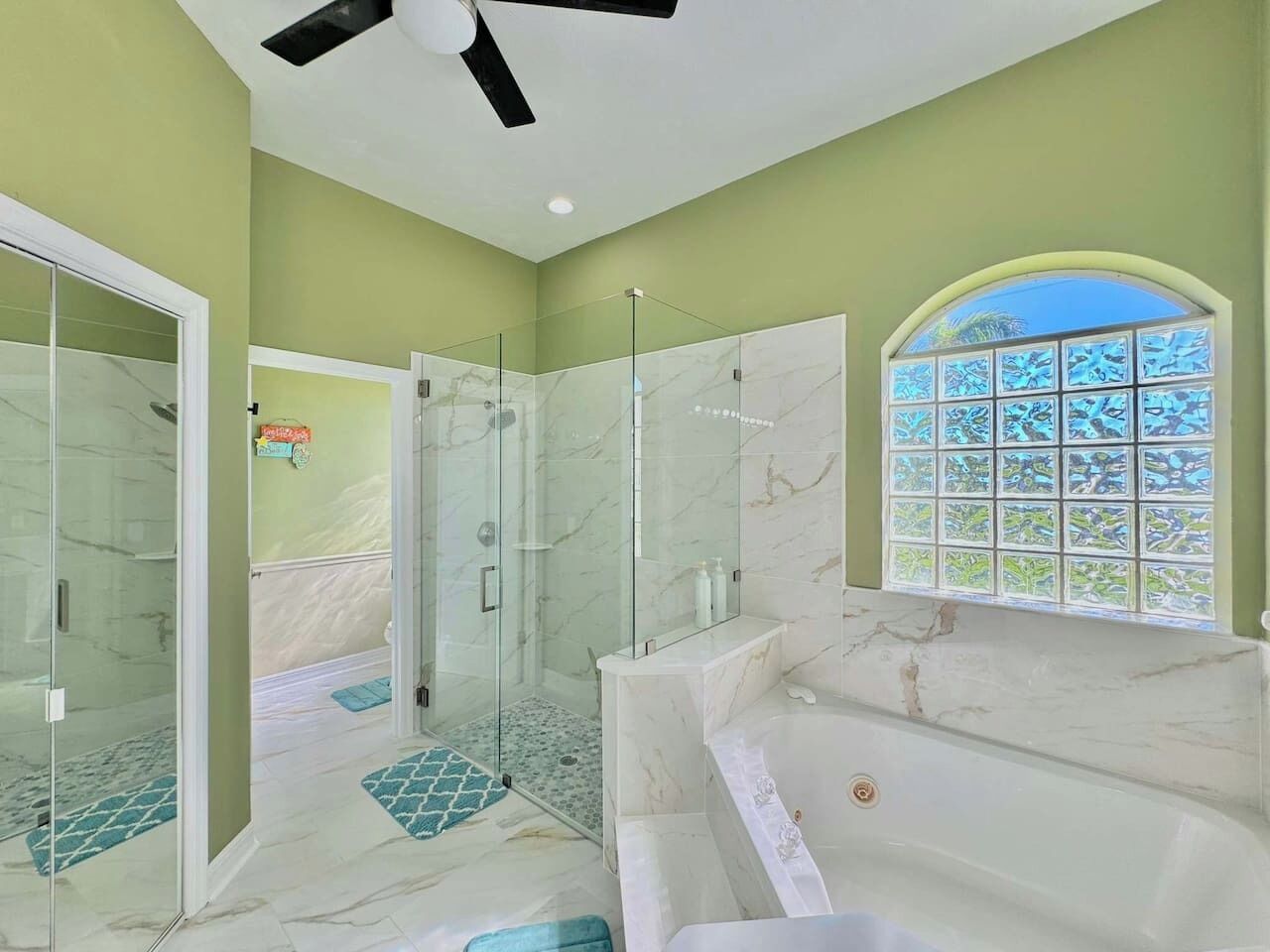 A modern bathroom with a glass-enclosed shower, a marble bathtub, and a window with a view.