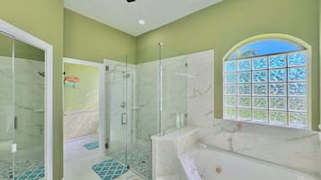 A modern bathroom with a glass-enclosed shower, a marble bathtub, and a window with a view.