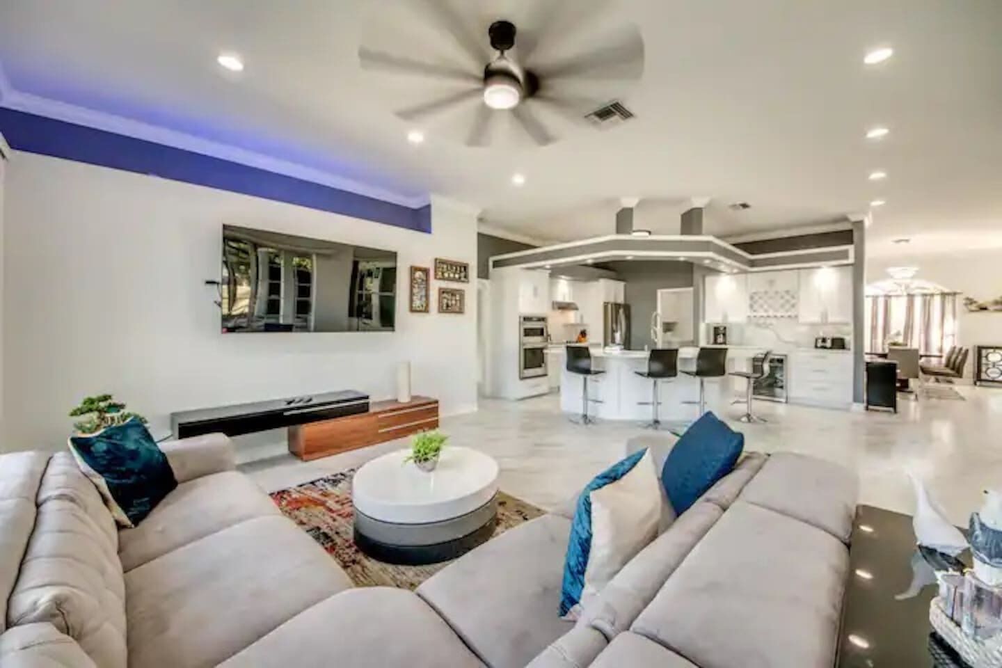 A modern living room with a sofa set, a coffee table, and a dining area with bar stools.
