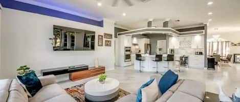 A modern living room with a sofa set, a coffee table, and a dining area with bar stools.