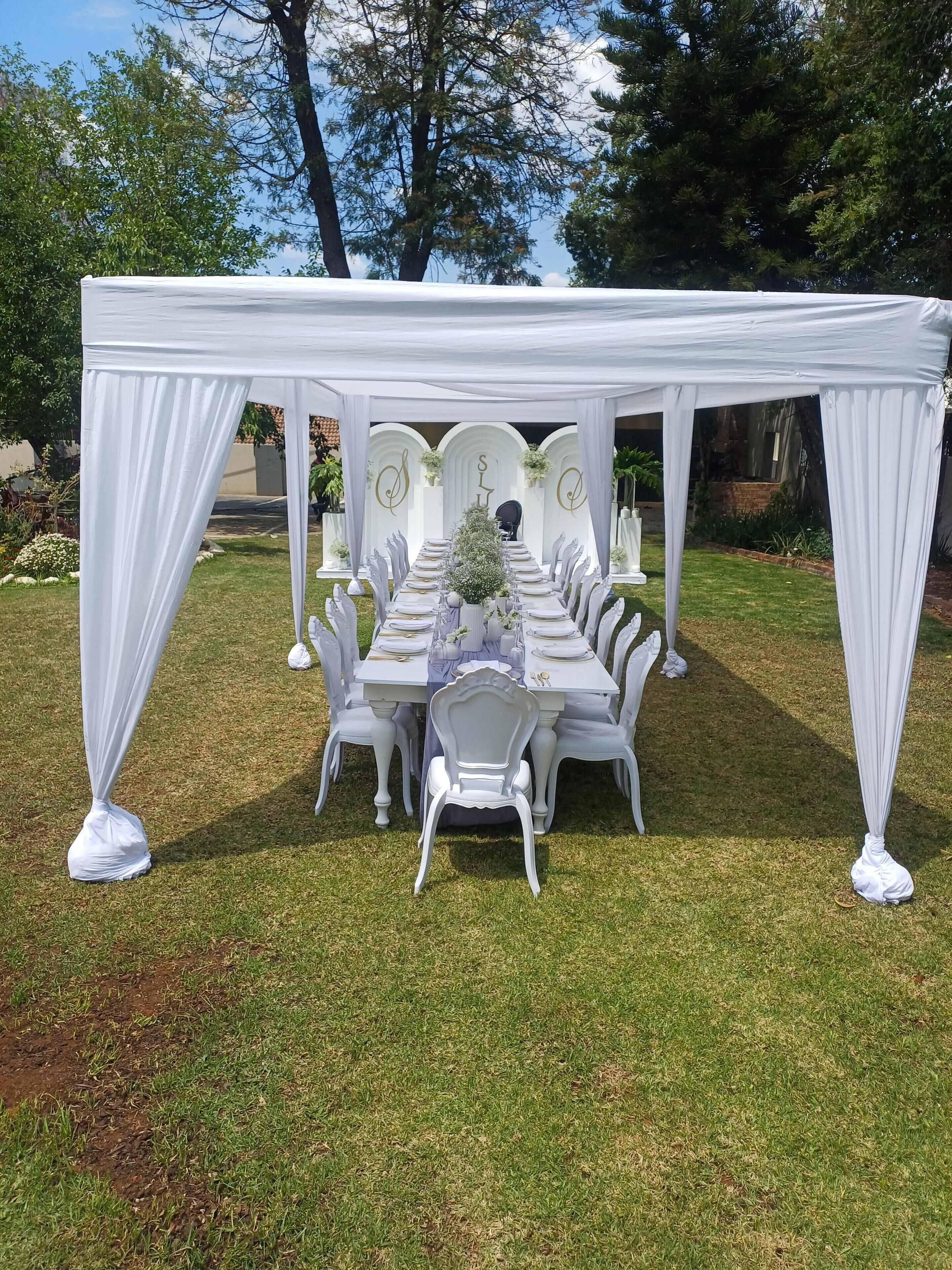 An outdoor dining area with white tables and chairs, covered by a white canopy.