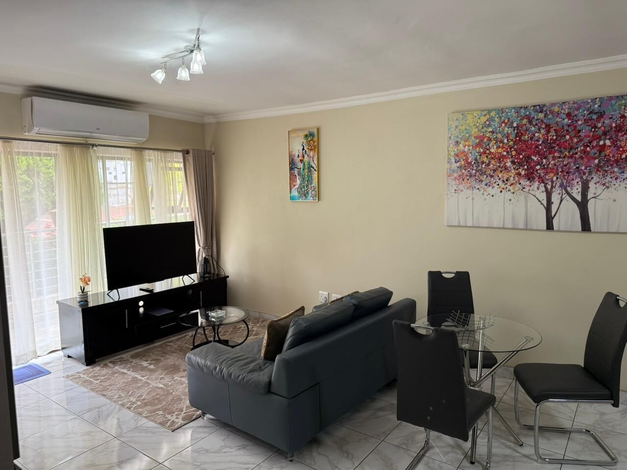 Uma sala moderna com sofá, televisão e mesa de jantar com cadeiras.