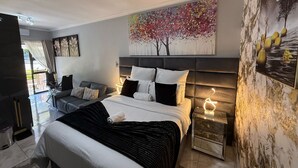 Une chambre moderne avec un grand lit, un canapé, un bureau et un tableau représentant un arbre.