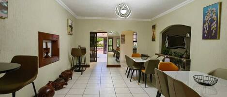 Un comedor amplio con una mesa larga y sillas, piso de baldosas y vista a otra habitación.