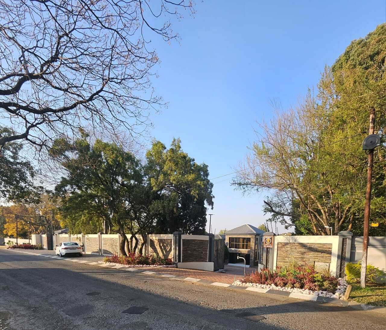 A gated residential area with a paved driveway, a white car parked, and a small building with a sloped roof.
