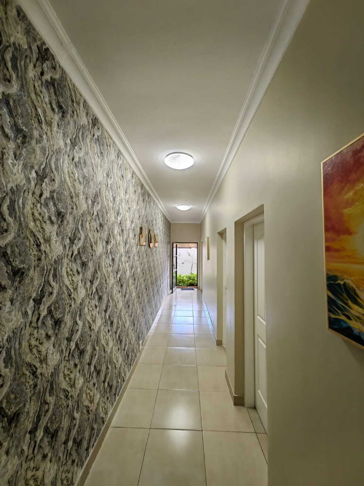 A hallway with a textured wall, recessed ceiling lights, and a door at the end.