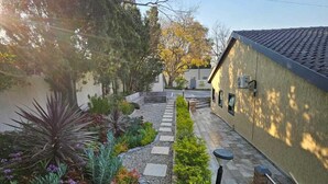 Une cour avec un chemin en pierre, diverses plantes et un bâtiment doté d’un toit en tuiles.