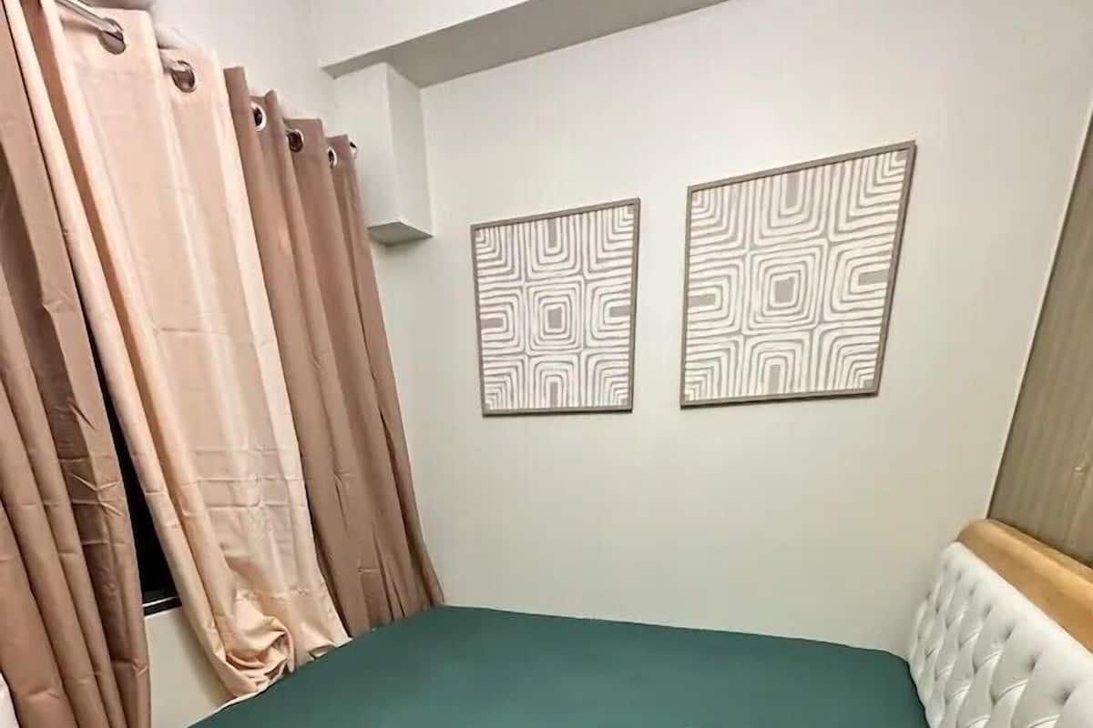 A bedroom with a bed, curtains, a furry rug, and two patterned wall decorations.