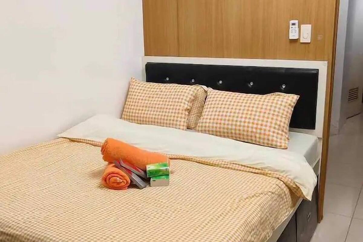 A neatly made bed with a checkered bedspread, a rolled towel, and a small item on the bed.