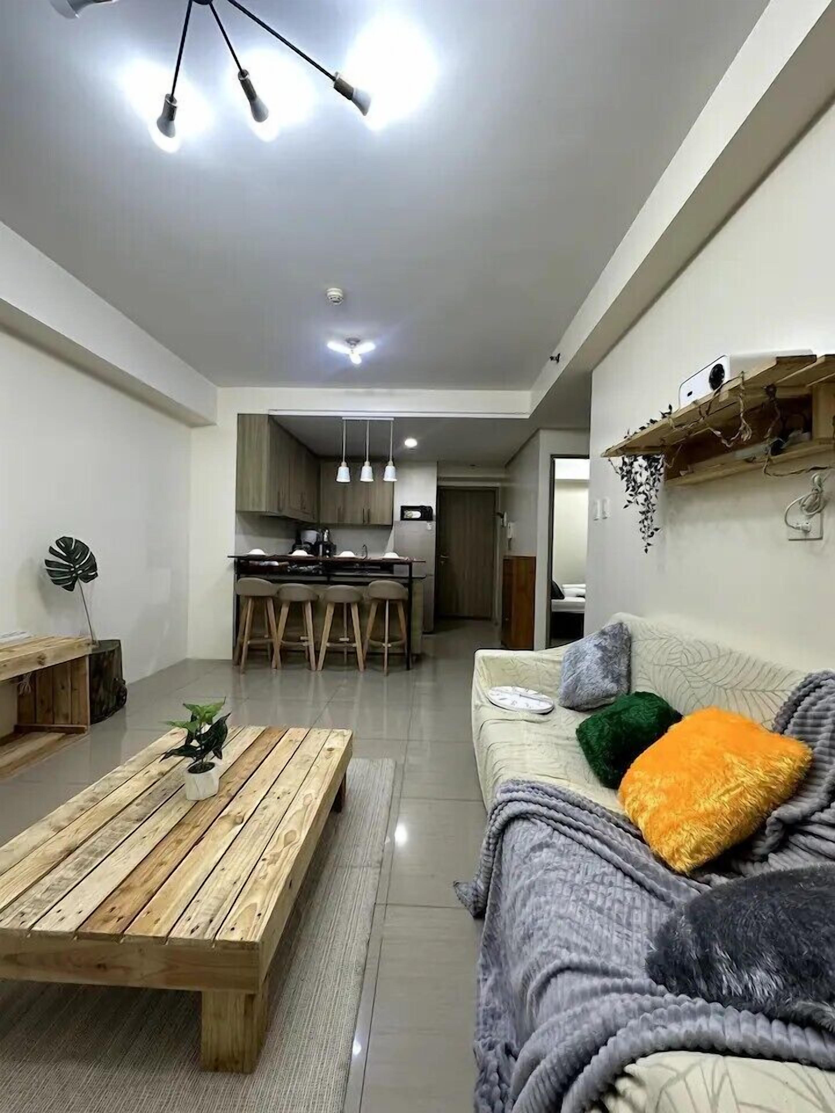 Una sala de estar moderna con una mesa de centro de madera, un sofá con cojines de colores y una cocina al fondo.