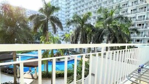A balcony with a view of a swimming pool, palm trees, and a high-rise building in the background. - House of Wu (Pasay)