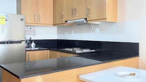 A compact kitchen with wooden cabinets, a black countertop, and a white table. - House of Wu (Pasay)