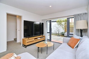 A modern living room with a flat-screen TV, a sofa, a coffee table, and a sliding glass door leading to an outdoor area.