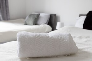 A neatly made bed with white bedding and pillows, a bedside table with a lamp, and a gray curtain in the background. - Leeds Retreat - 4BR House, Sleeps 10 (Leeds)