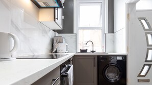 Eine kompakte Küche mit integrierter Waschmaschine und Trockner, einem Fenster und einer Arbeitsplatte mit Wasserkocher.