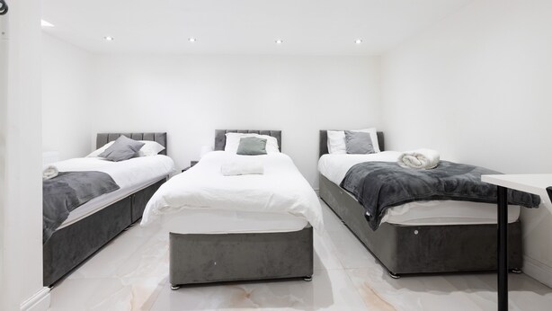 Ein modernes Schlafzimmer mit drei Betten, einem kleinen Tisch und einer weißen Decke mit eingelassener Beleuchtung.