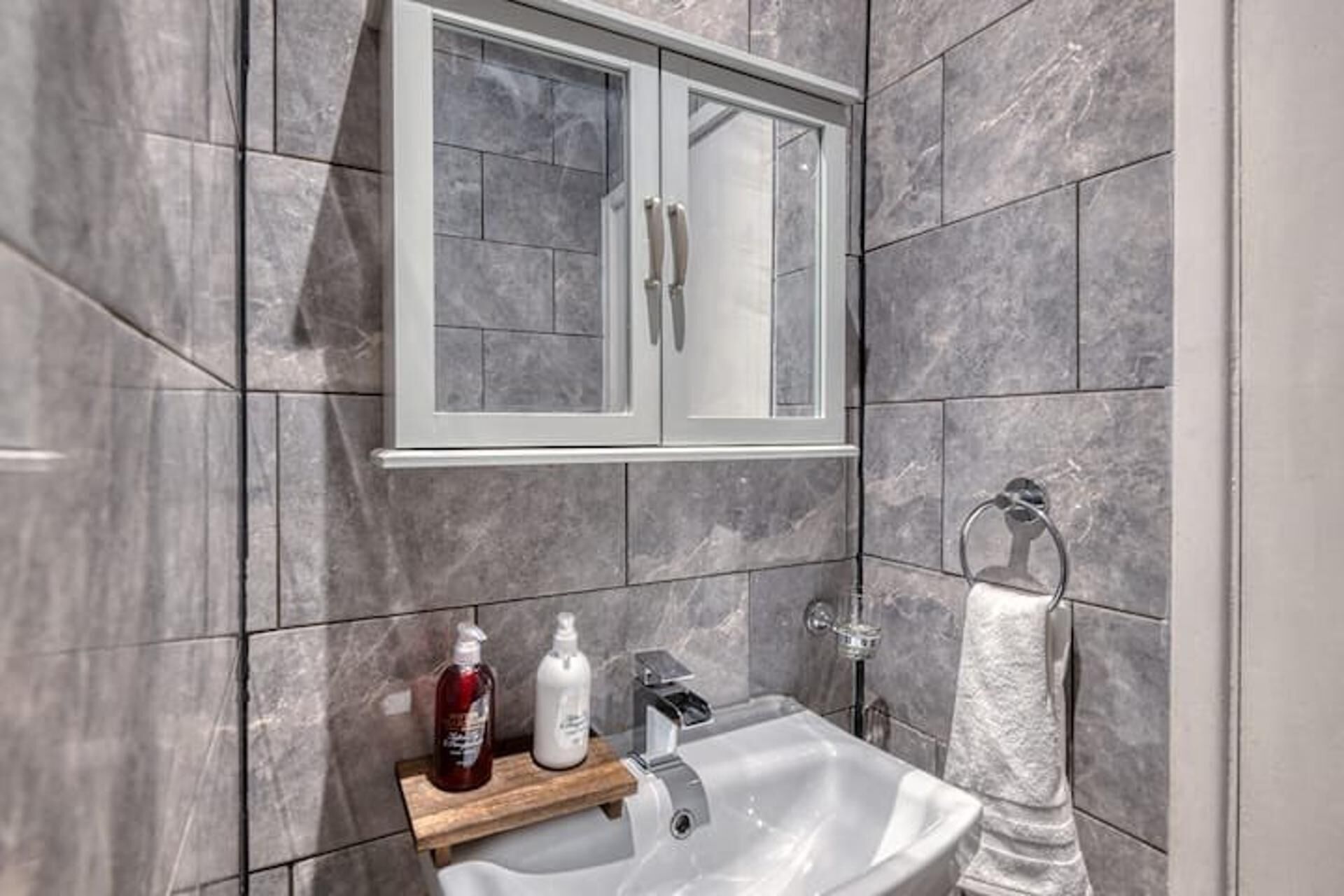 A bathroom with a marble wall, a white sink, a mirror cabinet, and a towel rack.